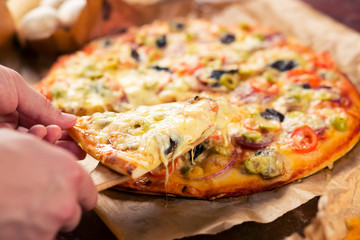 man takes a slice of hot freshly baked pizza with a lot of cheese Parmesan
