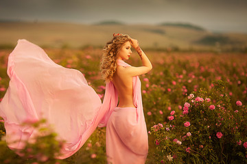 Fototapeta na wymiar beautiful sexy girl in a pink dress standing in the garden roses