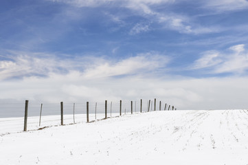 Fence in Snow Covered Field with Clouds and Blue Sky