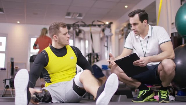  Man with prosthetic leg working out at the gym with personal trainer