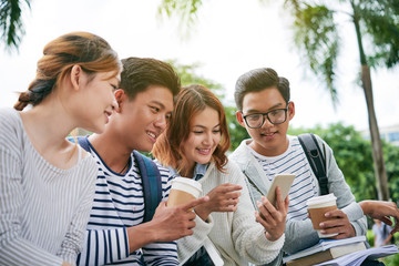 Cheerful classmates looking at screen of smartphone