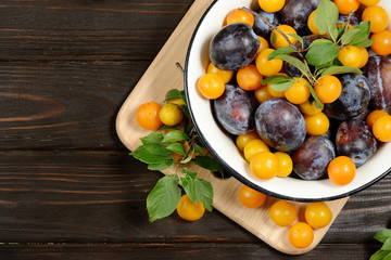 Fresh blue yellow plums in metal bowl on dark wooden table.