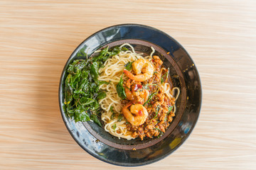 Instant noodles with Spicy fried shrimp and pork with chilli & Basil leaves in bowl on wooden background - Thai food

