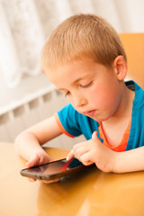 Young boy plays with a smart phone at kitchen table