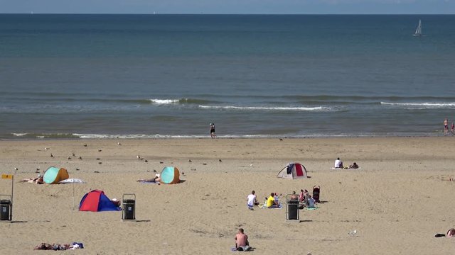 Footage of a North Sea beach showing the light brown colored sand the blue sea and the bright blue summer sky at background also showing people on beach enjoying the sun and landscape during vacation