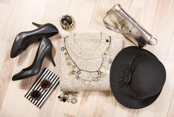 Winter sweater and accessories arranged on the floor. Woman sweater with silver accessories, high heels, hat, necklace and nail polish.