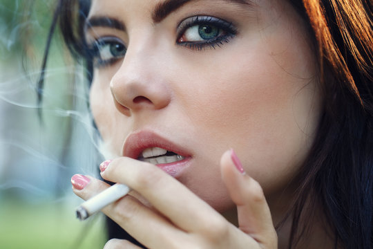 Closeup portrait of white Caucasian beautiful young sexy brunette woman with light blue green eyes smoking cigarette looking in camera, toned with Instagram filters, bad unhealthy habit