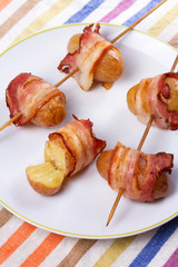 Bacon-wrapped potato in white plate.