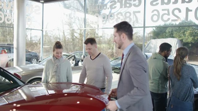 Salesman in car dealership with couple, showing them the engine of new car