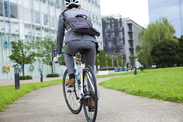 Back figure of businessman wearing a helmet while riding a bicycle