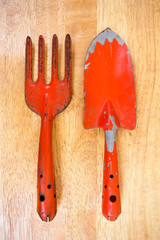 Small orange gardening shovel and fork on wooden board backgroun