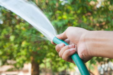 Holding a water hose to water the plants in the garden.