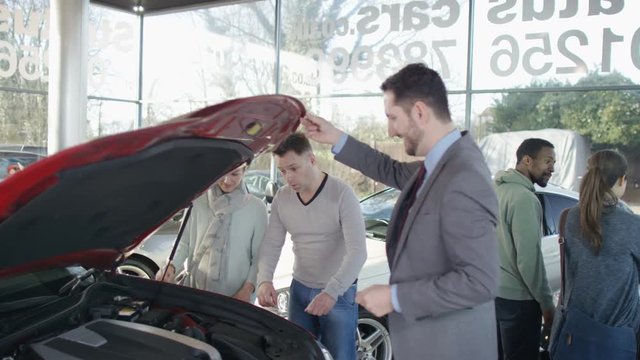  Salesman in car dealership showing couple new car & shaking hands on a deal. 