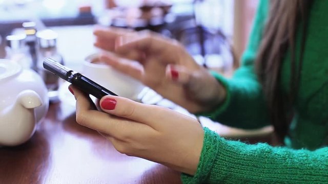Woman is using smartphone in a cafe, writing a message on the social network. Close up