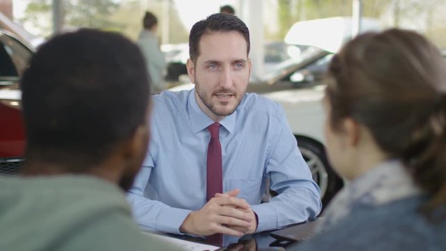  Happy couple in car dealership talking to salesman & taking key to new car