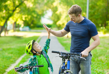 father and son give high five while cycling in the park