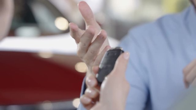  Close up on hands of salesman in car dealership giving key to new owner. 