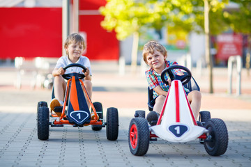 Two active little kid boys driving pedal race cars