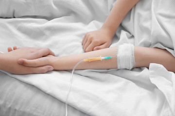 Mother holding daughter's hand with drip infusion