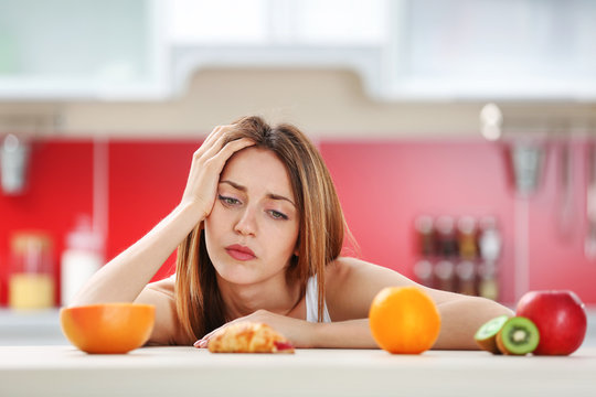 Woman looking guilty at croissant lying among fruits
