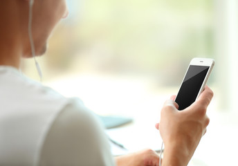 Young man listening to music on smartphone in the room
