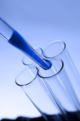 Close up of a pipette dropping a  sample into a test tube on blue background