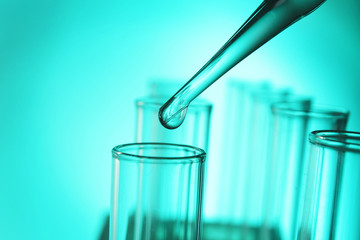 Close up of a pipette dropping a  sample into a test tube on turquoise background