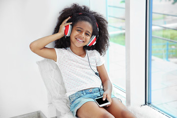 Fototapeta na wymiar Cute African American girl listening music on windowsill