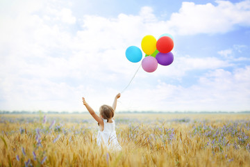 Little happy girl with balloons in the field