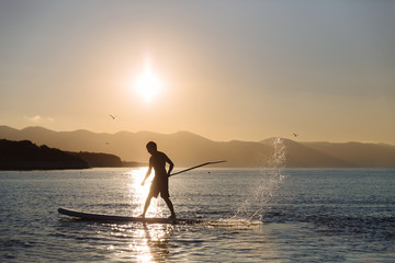 silhouette of young boy paddle boarding at sunset. concept  lifestyle sport