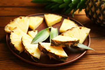 Pineapple slices and leaves in plate on wooden background