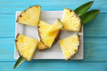 Pineapple slices and leaves in plate on blue background