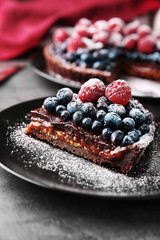 Piece of delicious chocolate tart with berries on black plate