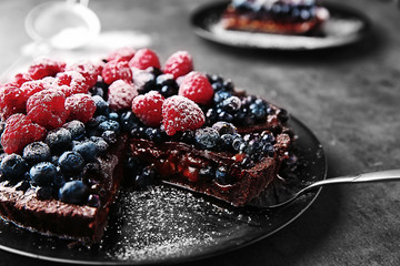 Delicious sliced chocolate tart with berries on black plate, closeup