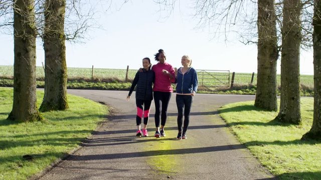  Female friends in fitness clothing walking together outdoors in countryside