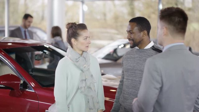  Happy couple in car dealers shake hands with salesman & take key to new car