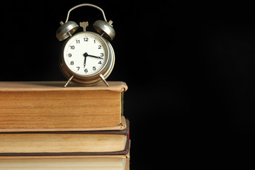 Naklejka premium Alarm clock on books and on a black background. The concept of time to read books