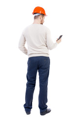 Backview of business man in construction helmet stands and enjoys tablet or using a mobile phone. Standing young guy. Rear view people collection.  backside view of person.  Isolated over white