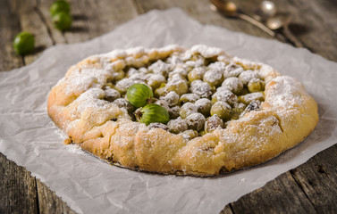 Galette with fresh berries. Gooseberry rustic tart on rough wooden background. Selective focus 