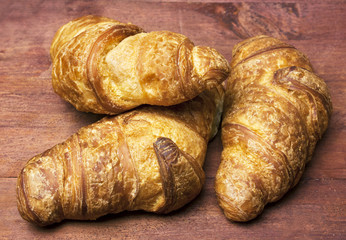 Photo of three appetizing croissants, shot on wooden texture