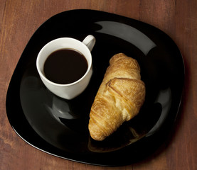 Cup of dark coffee with croissant on black plate