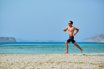 Fototapeta na wymiar strong athletic man with bared torso running on the beach along the sea front