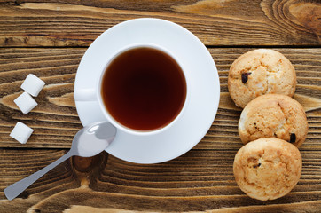 Cup of tea on a wooden table, sugar, spoon, cookies, top view