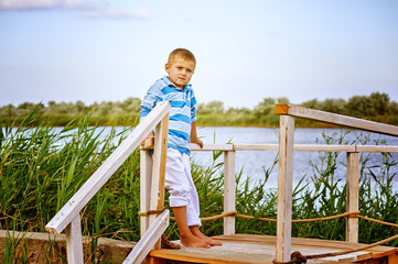 beautiful boy posing on a wooden bridge . Dressed in a nautical style .