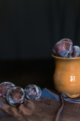 plums on a dark background in a glass vase clay blue summer berry fruits