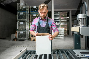 Handsome packer in working apron with box on the packaging line at the manufacture.