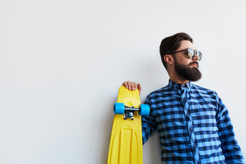 bearded hipster in checkered shirt holding yellow skateboard