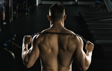 Fototapeta na wymiar brutal, athletic, muscular man posing in the gym with a naked back and a chain around the neck