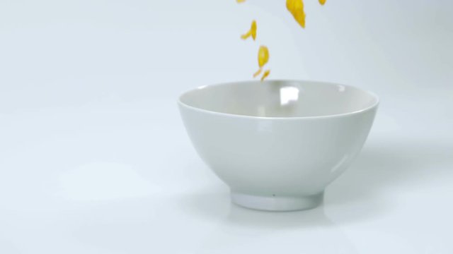 Corn flakes are falling into an empty cup which is standing on the table. Someone will eat this for his breakfast. Close-up shot.
