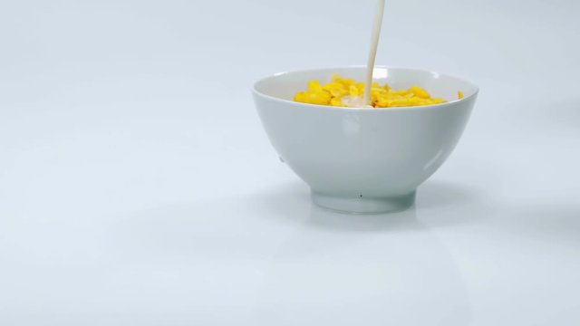 Someone is pouring some milk into a cup which is already full of corn flakes. This is a delicious and very healthy breakfast. Close-up shot.
